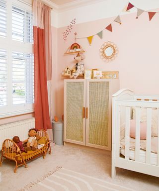 Pink nursery with pink painted wall, cream carpet and rug, white crib with pink painted rattan cabinet
