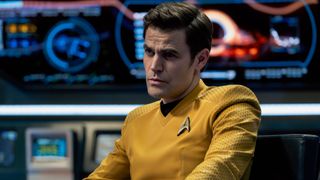 Captain Kirk sitting aboard the Enterprise in his classic yellow uniform in the Season 4 finale of Star Trek: Strange New Worlds. He has an intense stare. 