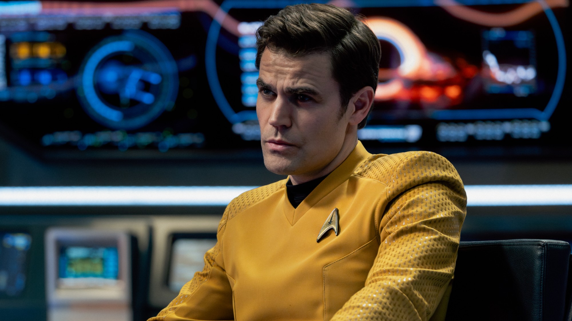 Captain Kirk sitting aboard the Enterprise in his classic yellow uniform in the Season 4 finale of Star Trek: Strange New Worlds. He has an intense stare. 
