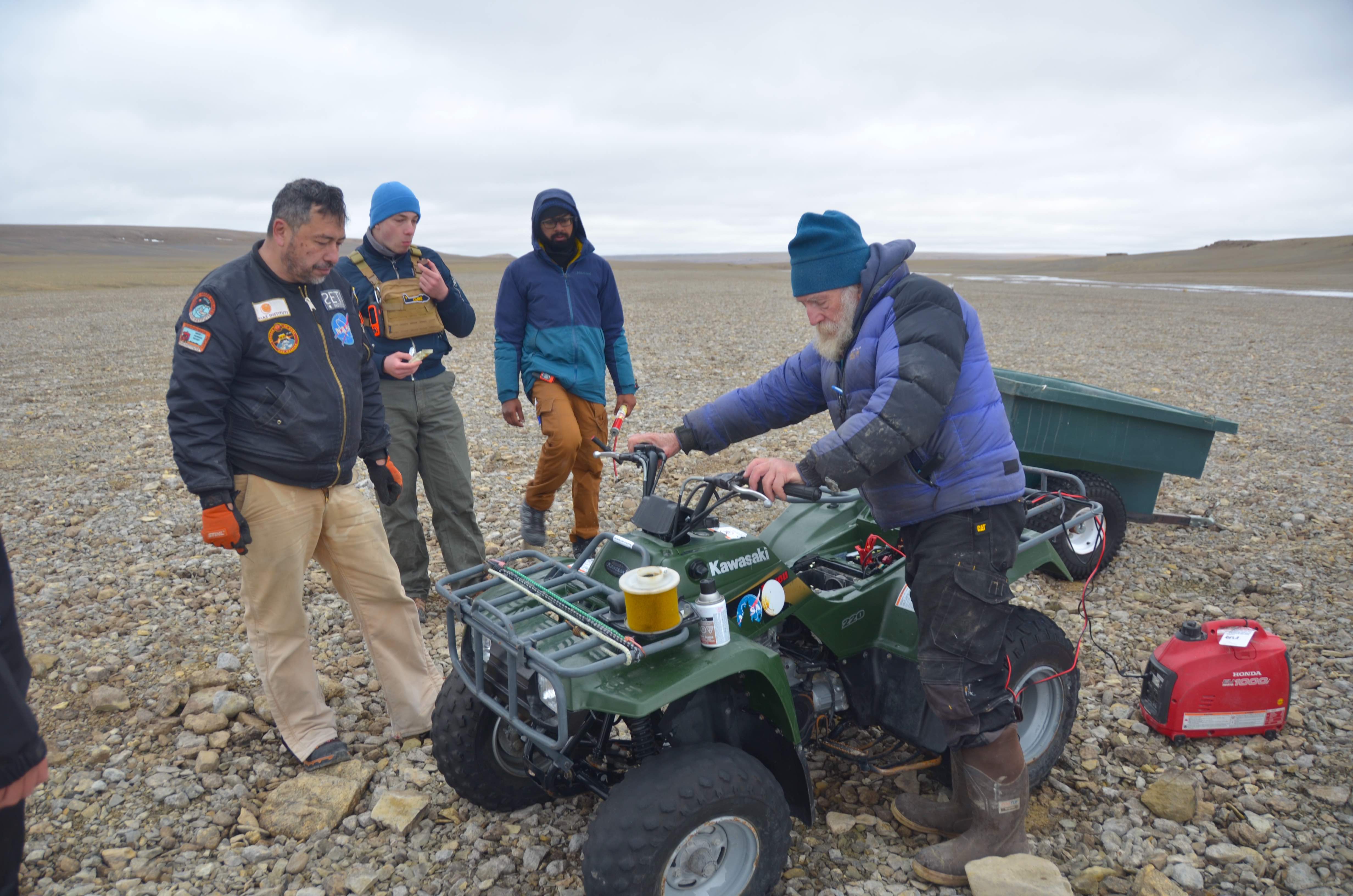 Three men watch another man on an ATV at the Haughton-Mars Project in the Arctic.
