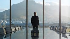 A businessman looks out the window of a conference room overlooking a mountain.