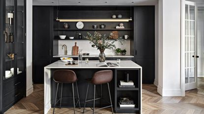 Kitchen with wooden flooring, black and cream fitted units, bar stools by the breakfast bar, high ceilings and coving.