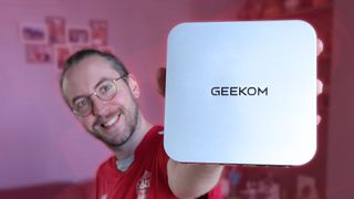 Windows Central Senior Editor Ben Wilson holding a Geekom A8 Max mini PC with a red background