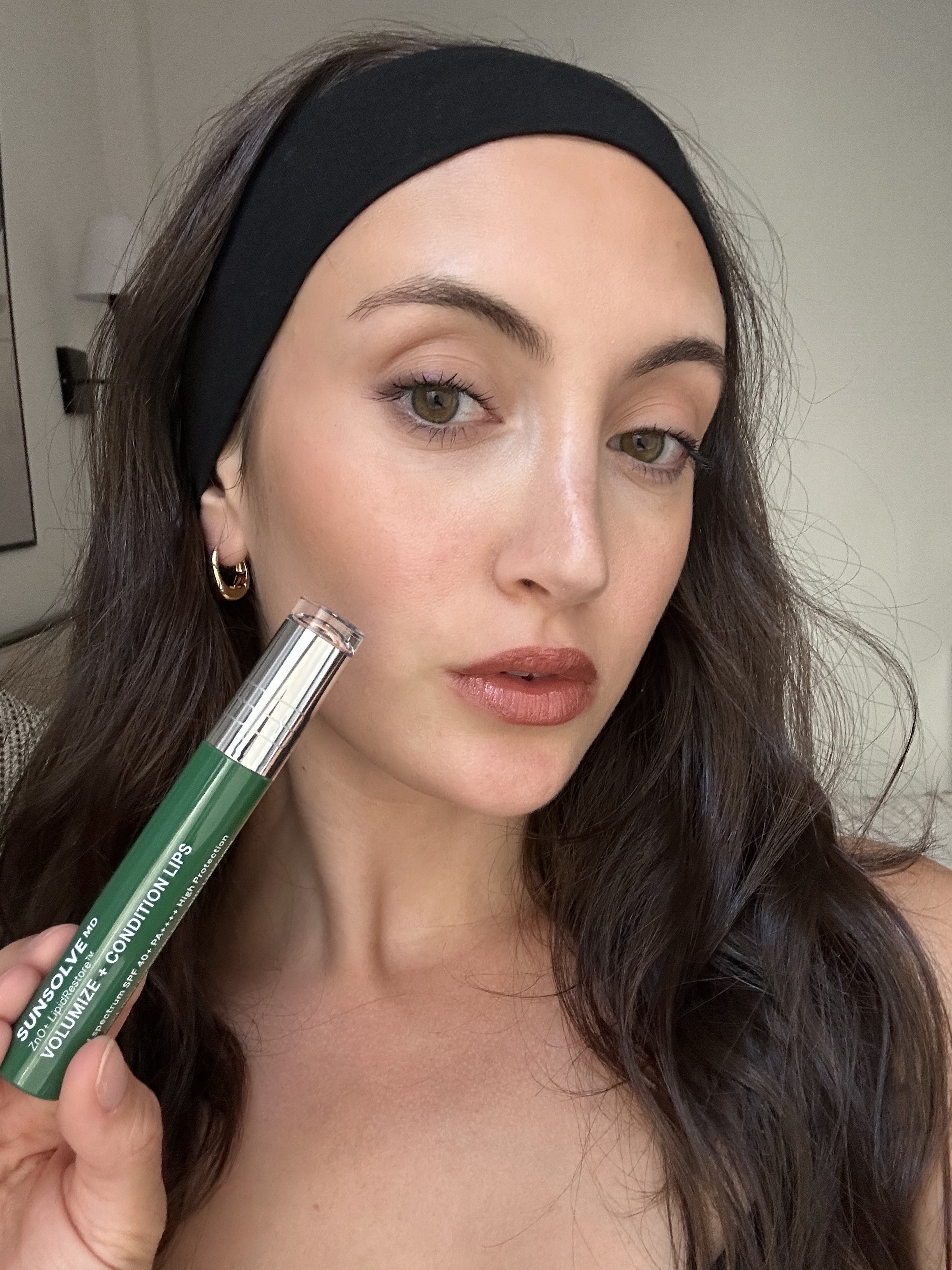 An image of Alyssa Brascia holding and wearing the SunSolve MD LipidRestore Volumize + Condition SPF 40.