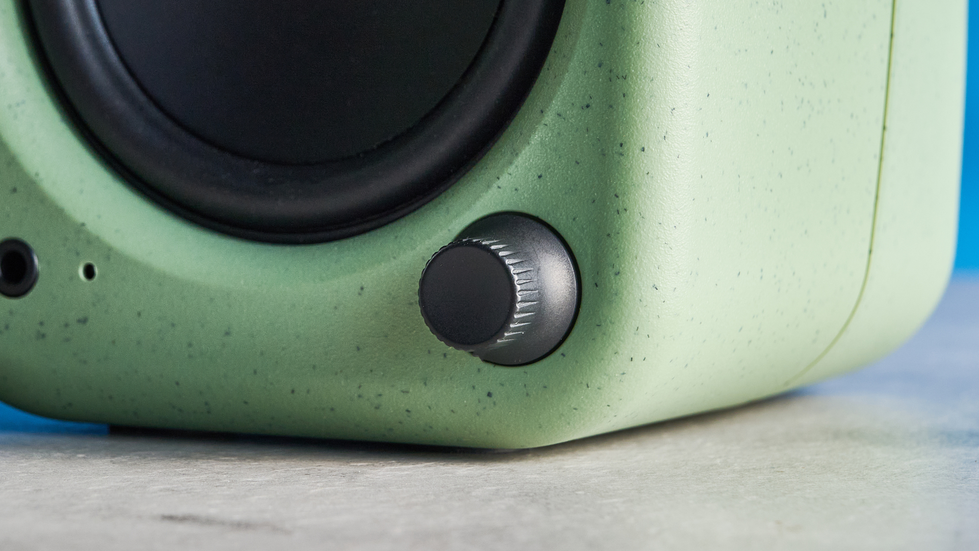 Kanto UKI bookshelf speakers in sage photographed in front of a blue background
