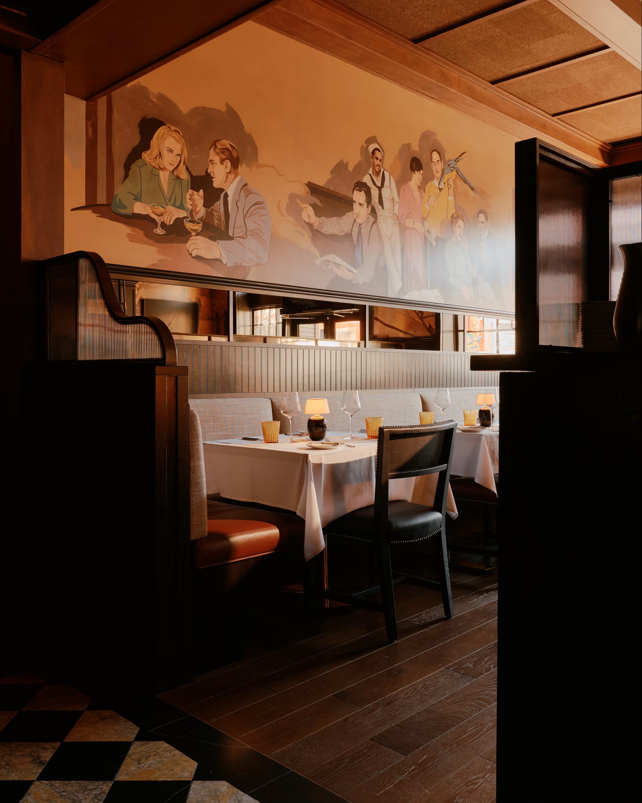 A warm-infused restaurant with murals capturing people dining, wooden ceilings and floors, checkered tiling, an bistro-style tables and chairs in wood and leather.