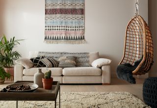 Cream living room ideas: boho-inspired cream living room with fabric wall hanging and rattan hanging chair in corner. Coco sofa