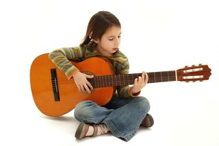 A young girl practices playing her guitar