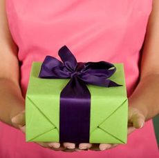 woman in pink dress holding gift wrapped in green with purple ribbon