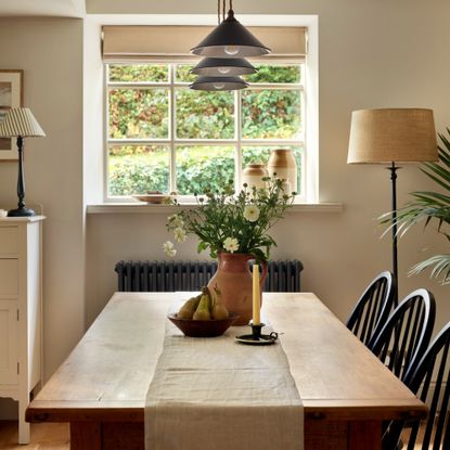A rustic-style dining room with a wooden rectangular dining table, three pendant lights above it, a floor lamp in the corner and a table lamp on a dresser nearby