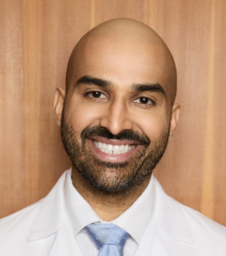 a man with a black beard in a white lab coat smiling at the camera
