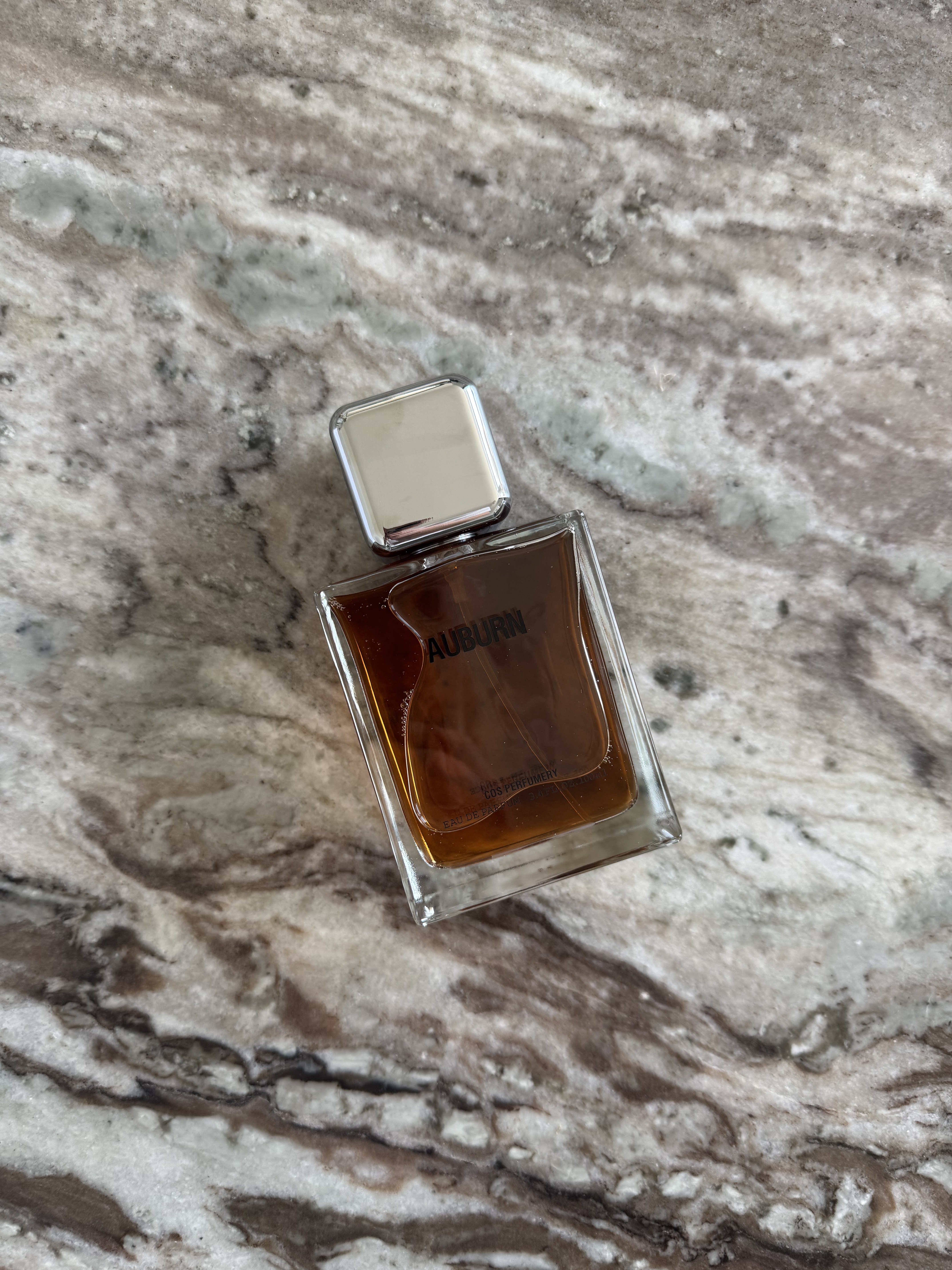 A photo of Cos Auburn perfume bottle on a marble table