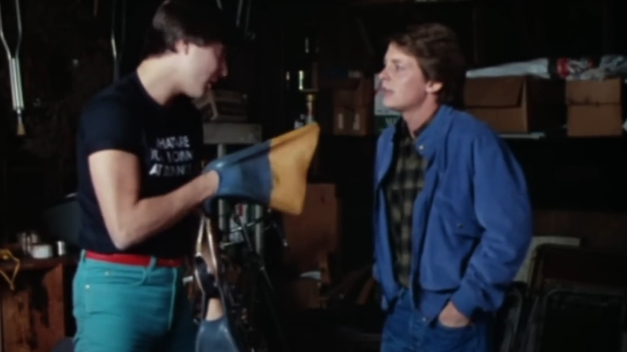 Jerry Levine points a flipper at Michael J. Fox while standing in the garage in Teen Wolf.