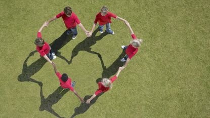 Aerial view of six children wearing red T-shirts and holding hands to form a heart shape.