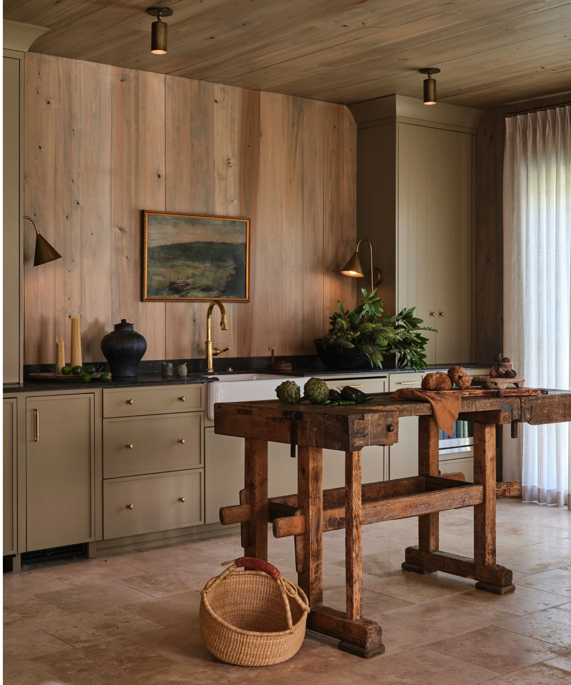 a rustic wood clad pool house kitchen with an antique table at the center and earthy green cabinetry