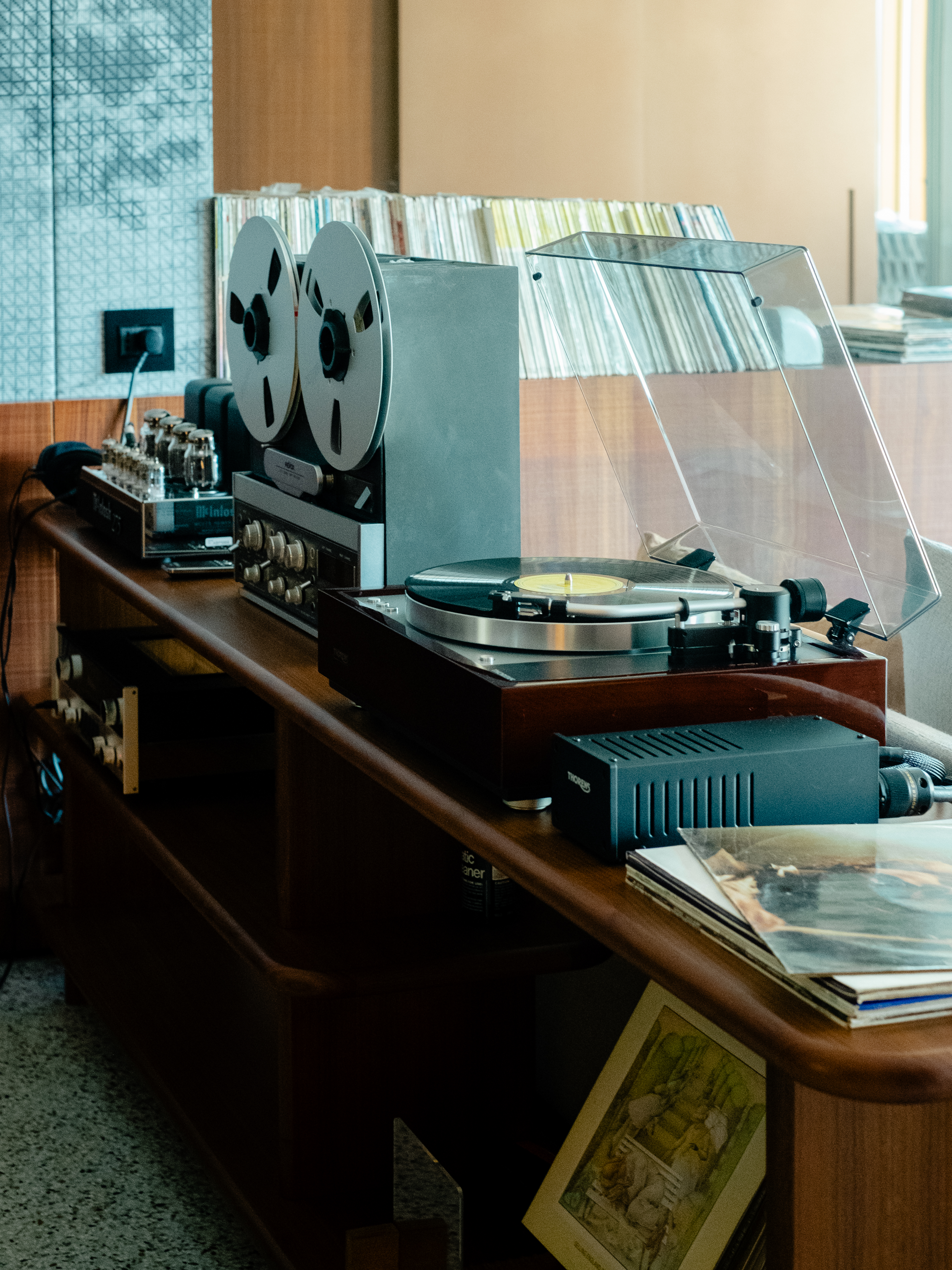 A high-fidelity listening suite fitted with retro-inspired music gear features floor-to-wall windows capturing the natural beauty of a lake and mid-century furniture with natural hues and textural furnishings.
