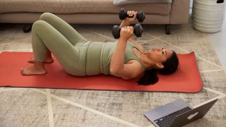 Woman holding dumbbells on yoga mat at home