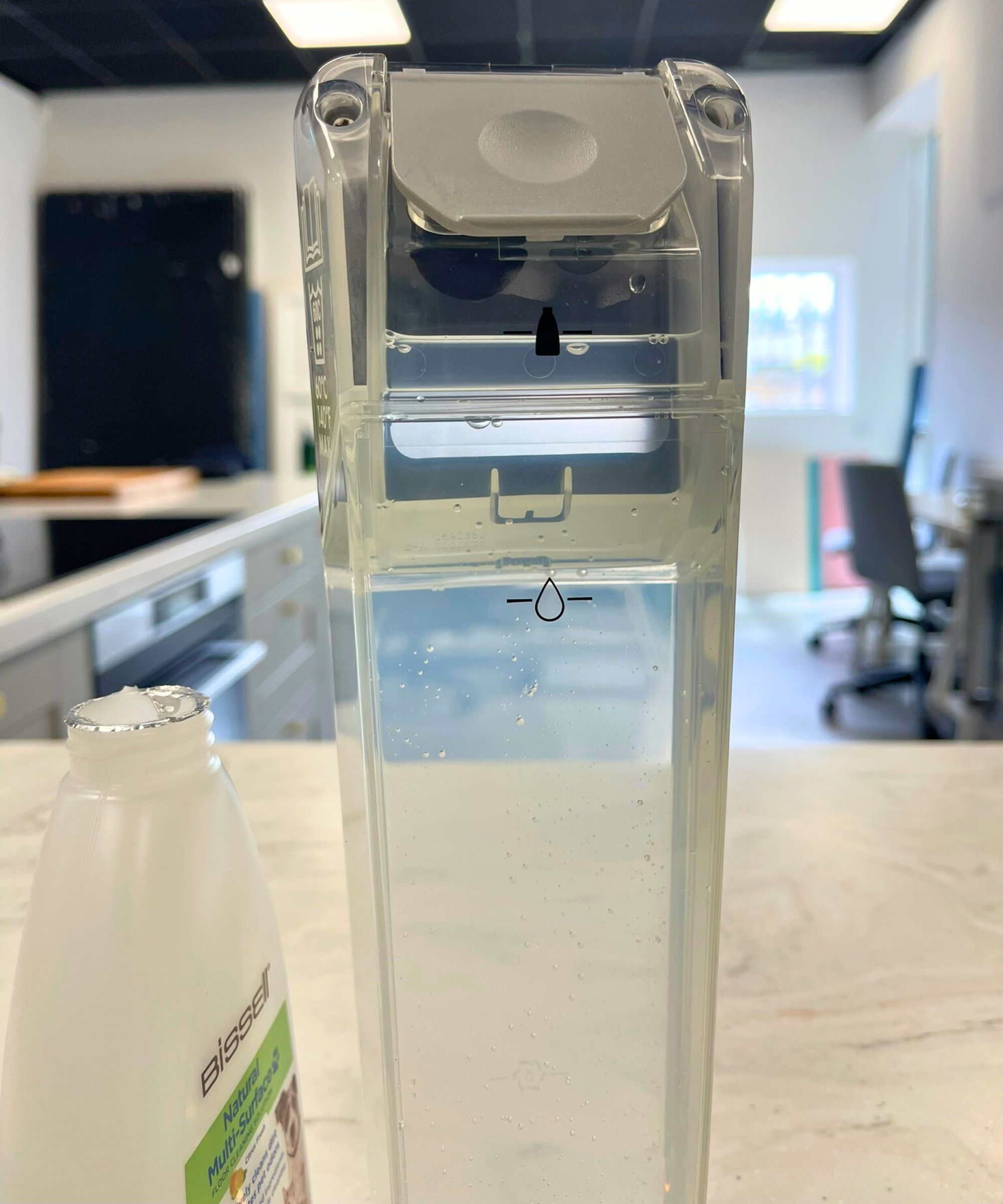 Closeup of Bissell CrossWave OmniForce Edge clean water tank next to Bissell cleaning solution, on marble counter in Future test center.
