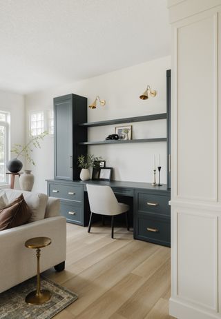 A living room with a build-in desk area with woodwork painted a blue-gray color