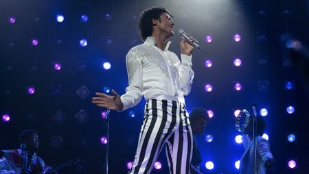 Jaafar Jackson singing on stage as Michael Jackson in a white top and striped pants in Michael movie 