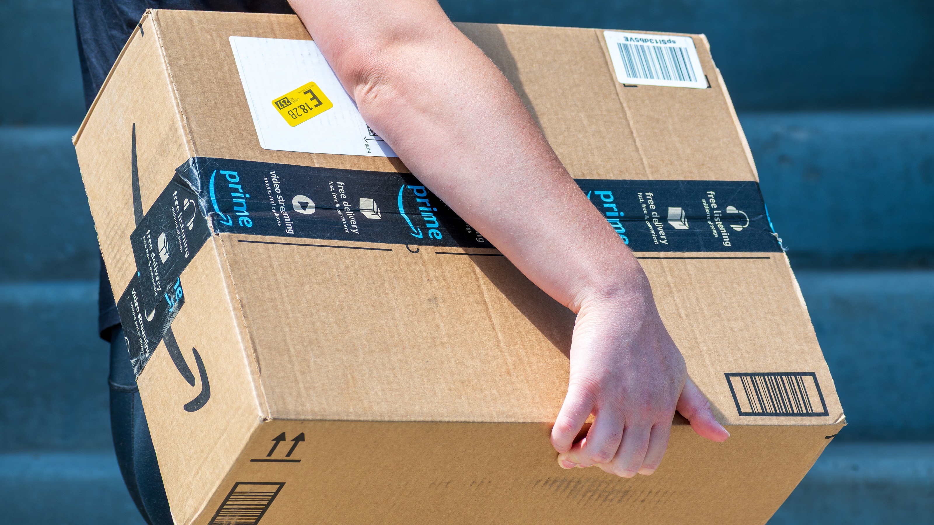 An Amazon box is carried by a person, only their arm showing.