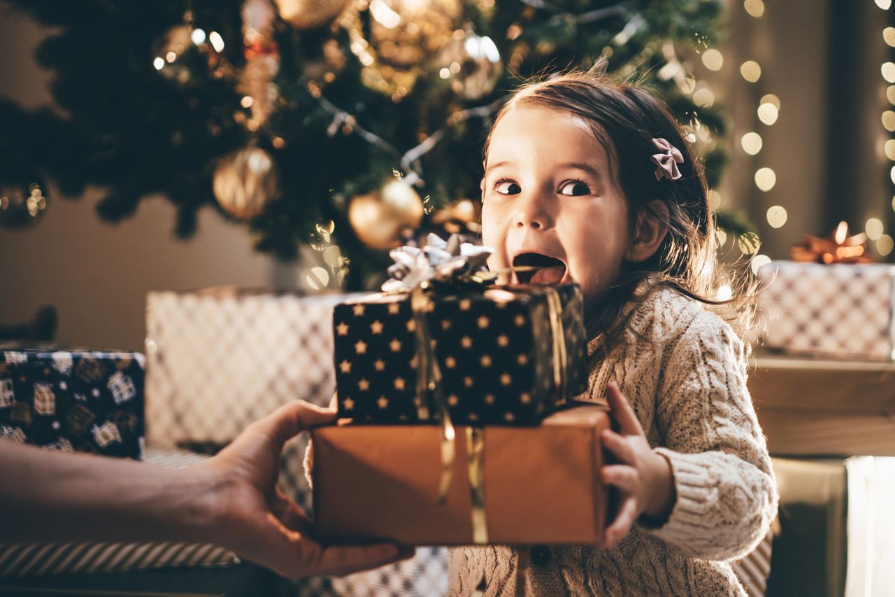 Young child receives Christmas presents with tree in background