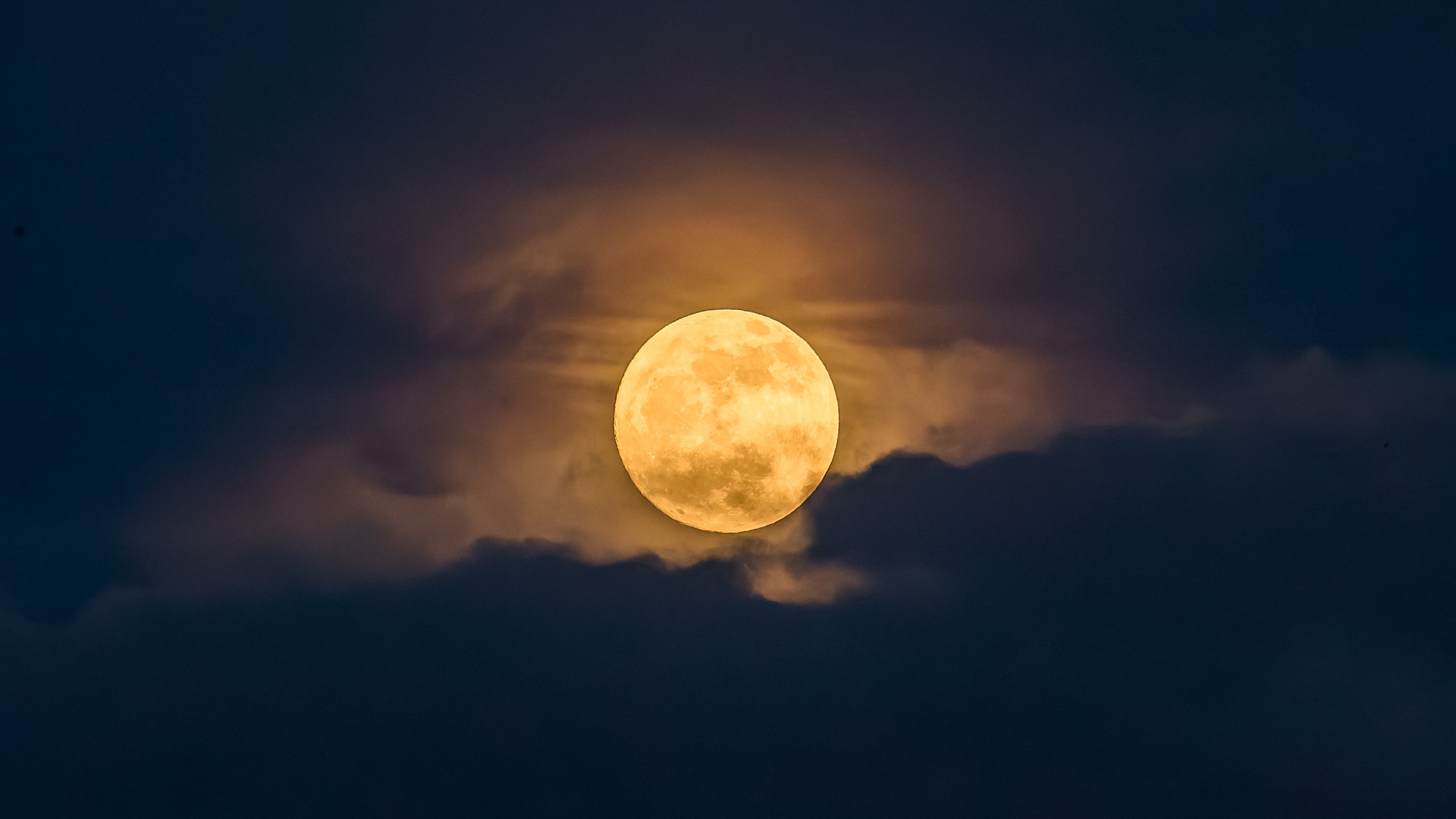 a light yellow hued moon shines behind a thin layer of cloud. The whole scene looks like a delicate painting.