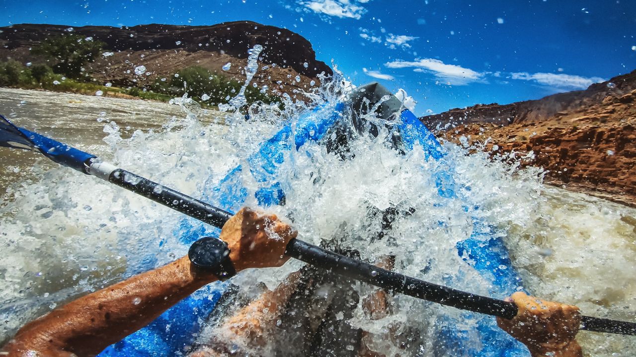 A man&#039;s hands hold an oar while he navigates rough water in a kayak.