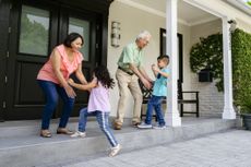 Cheerful Latin American senior couple welcoming home their energetic grandchildren on the front porch.