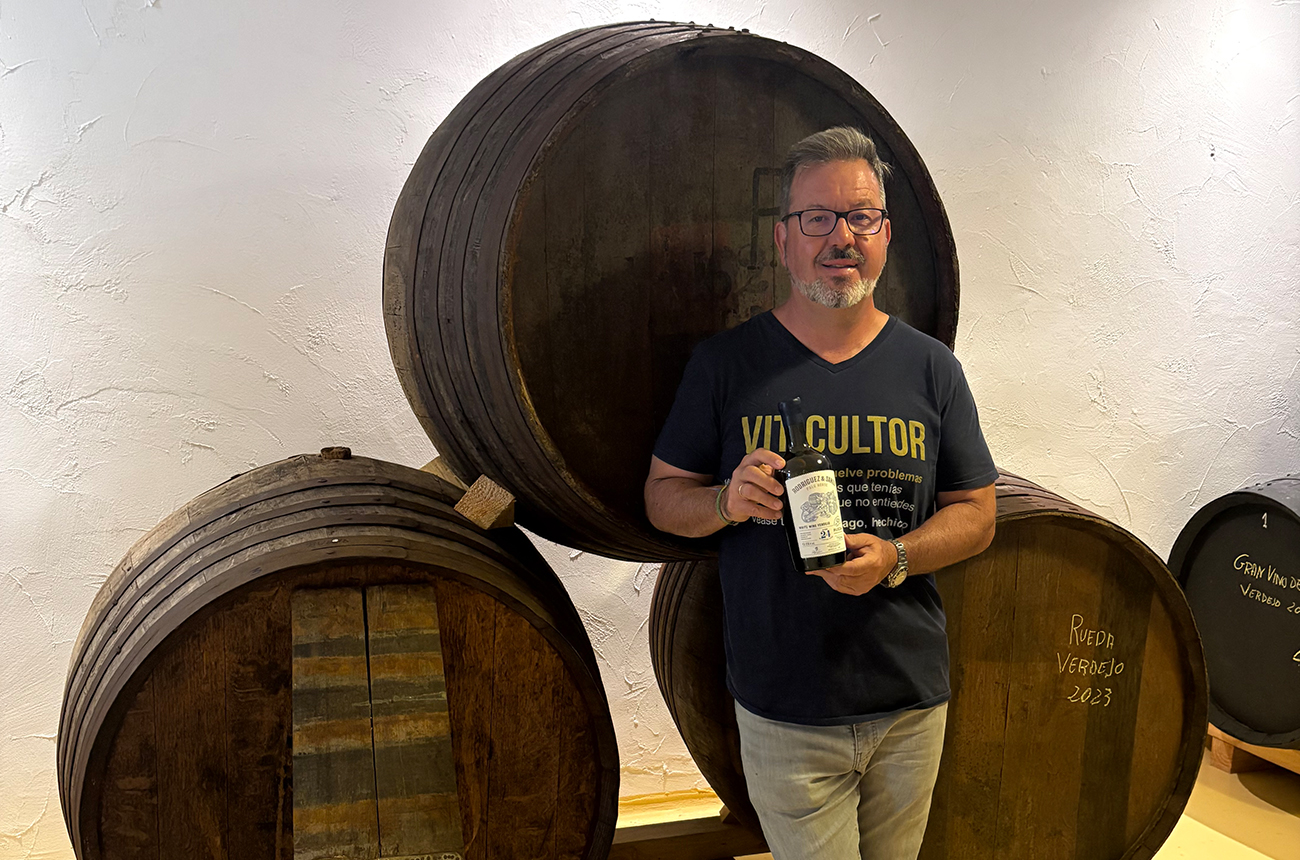 Javier Rodr&amp;iacute;guez, standing in front of a stack of three wooden barrels, holding a bottle of wine