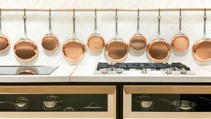 Luxury kitchen with copper pans hung on the wall, white tiled backsplash and white countertop with green and gold range