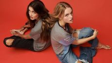2 women sitting on the floor looking up to the camera. They're wearing ripped jeans from Lucky Brand