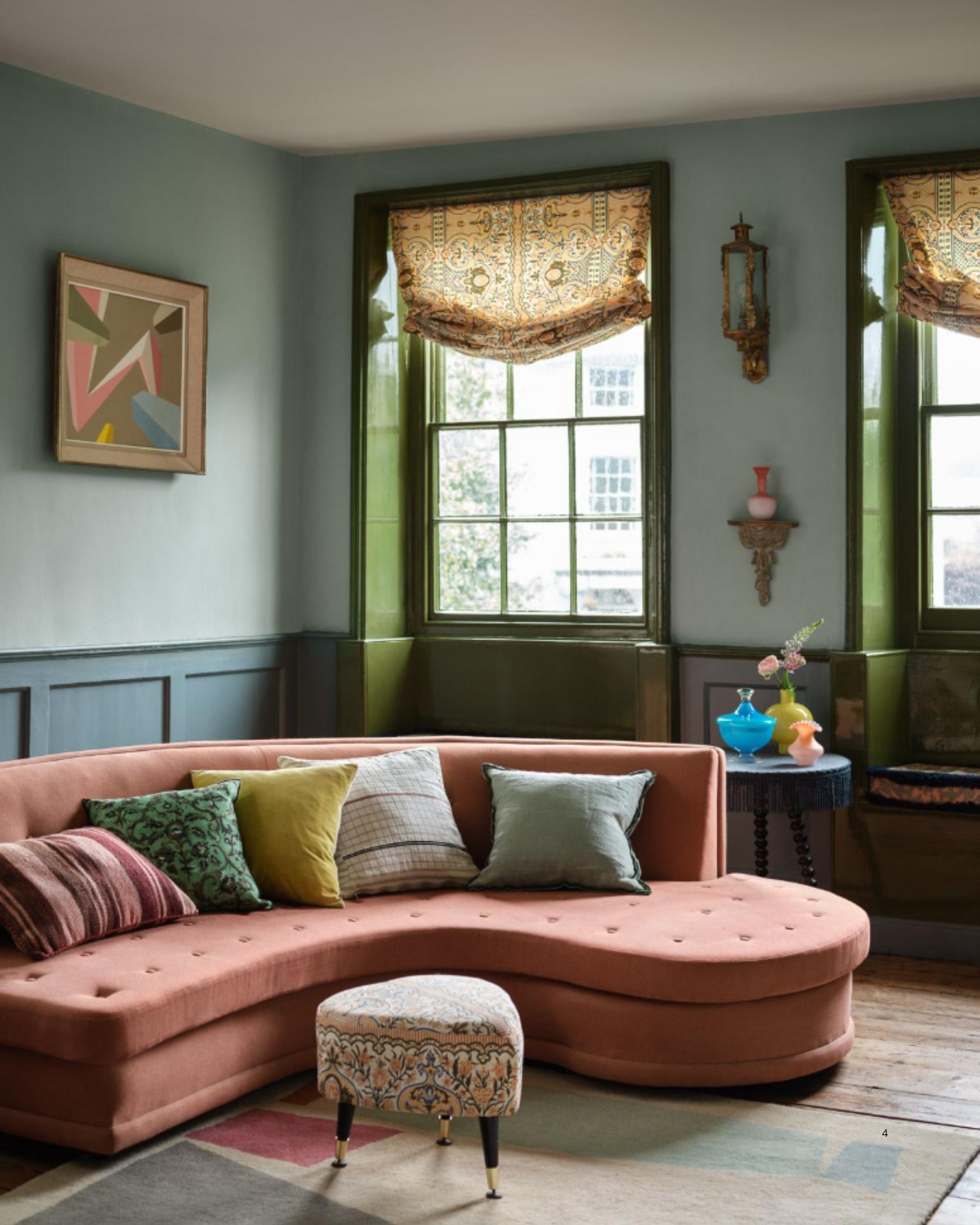 A light blue and navy colorblock living room with glassy green window frames and a curved coral pink sofa.