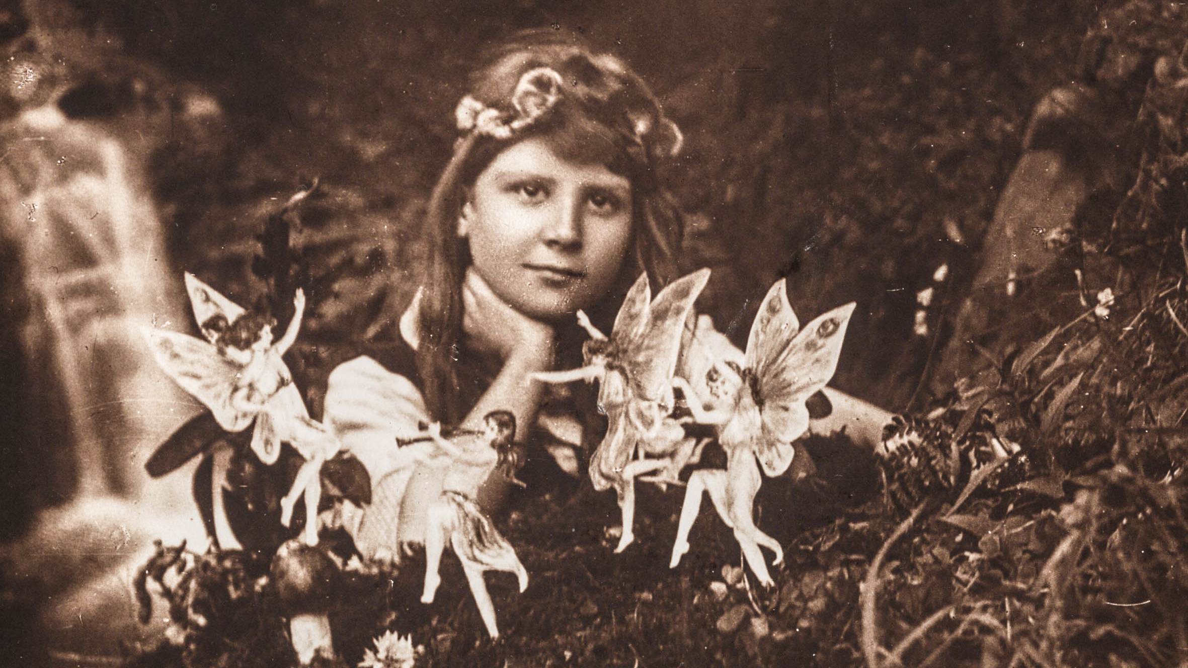 ENGLAND : A photograph of Frances 'Alice' Griffiths (1907-1986) taken by her cousin Elsie 'Iris' Wright (1901-1988), using her father Arthur's Midg quarter-plate camera, the first in the 'Cottingley Fairies' series. Frances, posed in the family garden, stares into the camera past dancing fairies, one of whom plays a pipe. A small waterfall tumbles into a 'beck', beyond. The fairies were actually drawings by Elsie, secured in the ground with hat pins. It was a secret the girls decided to keep until the 1980s - once they realised the extent of the deception - to protect the public reputations of those who believed in the 'truth' of the images. Alice was probably the name given to Frances by Sir Arthur Conan Doyle (1859-1930) in an attempt to conceal the girls' identities when he published the photographs. (Photo by SSPL/Getty Images)