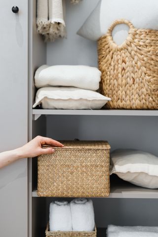 A wicker box placed inside closet with clothes and towels
