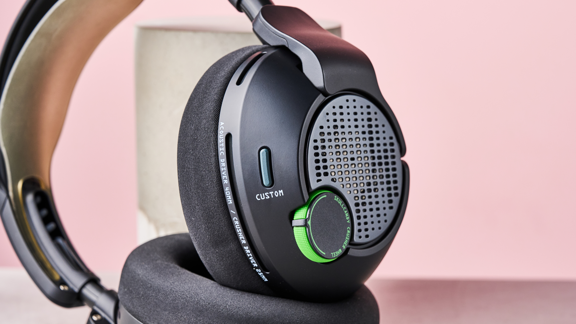 Close-up of outside of right-hand driver of Skullcandy Crusher PLYR 720, leaning on plinth on desk against a pink background