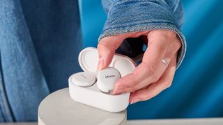 the denon perL Pro wireless earbuds in white, with circular earbud shapes, and a white charging case, photographed against a blue background