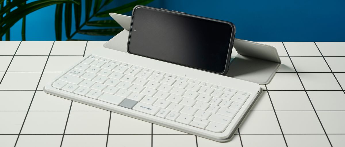 a google pixel phone connected via bluetooth propped up a white, lightweight tablet keyboard made by mokibo rests upon a white tiled table with a blue background