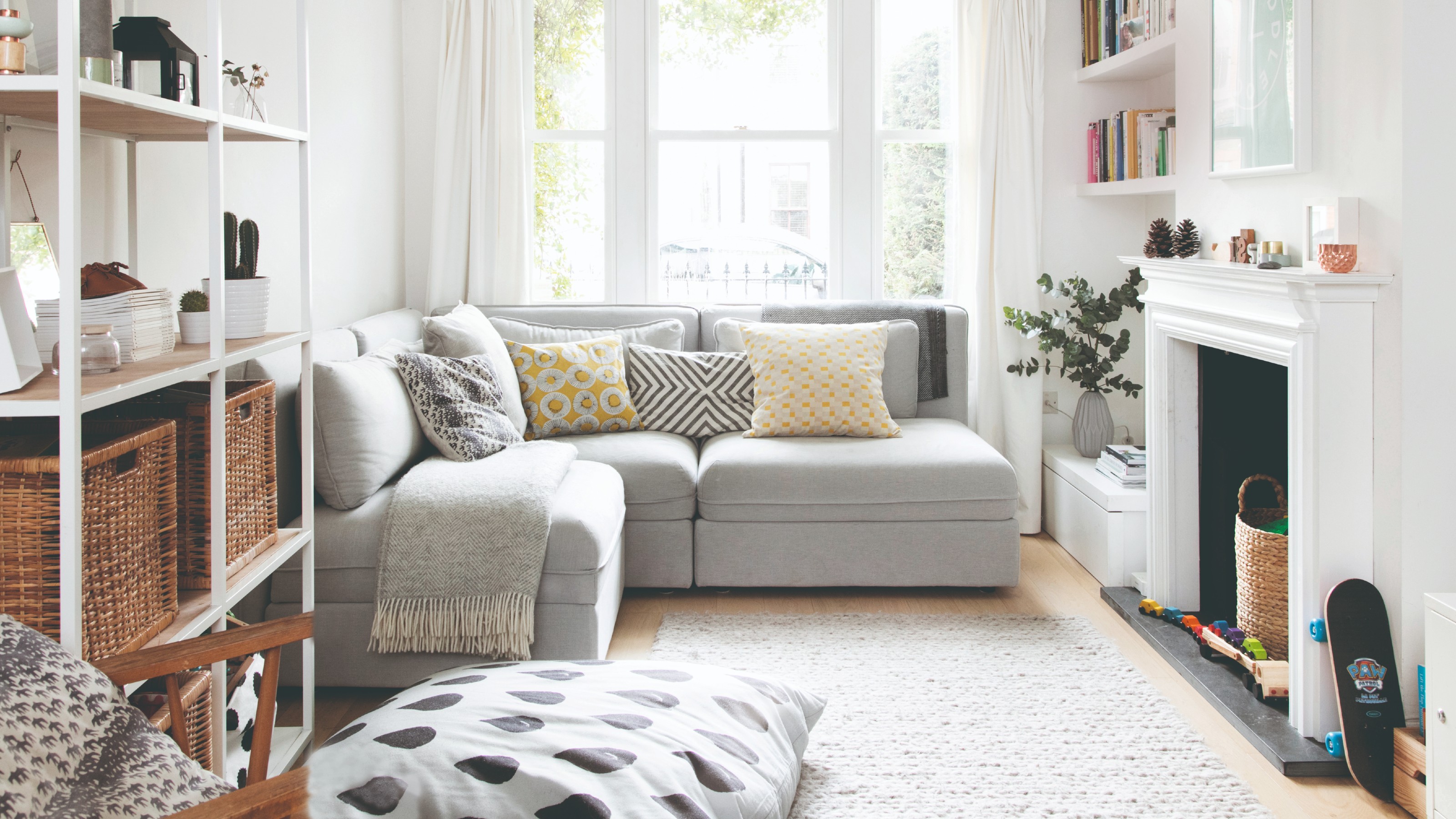 A white family living room with a modular corner grey sofa and shelving with storage baskets