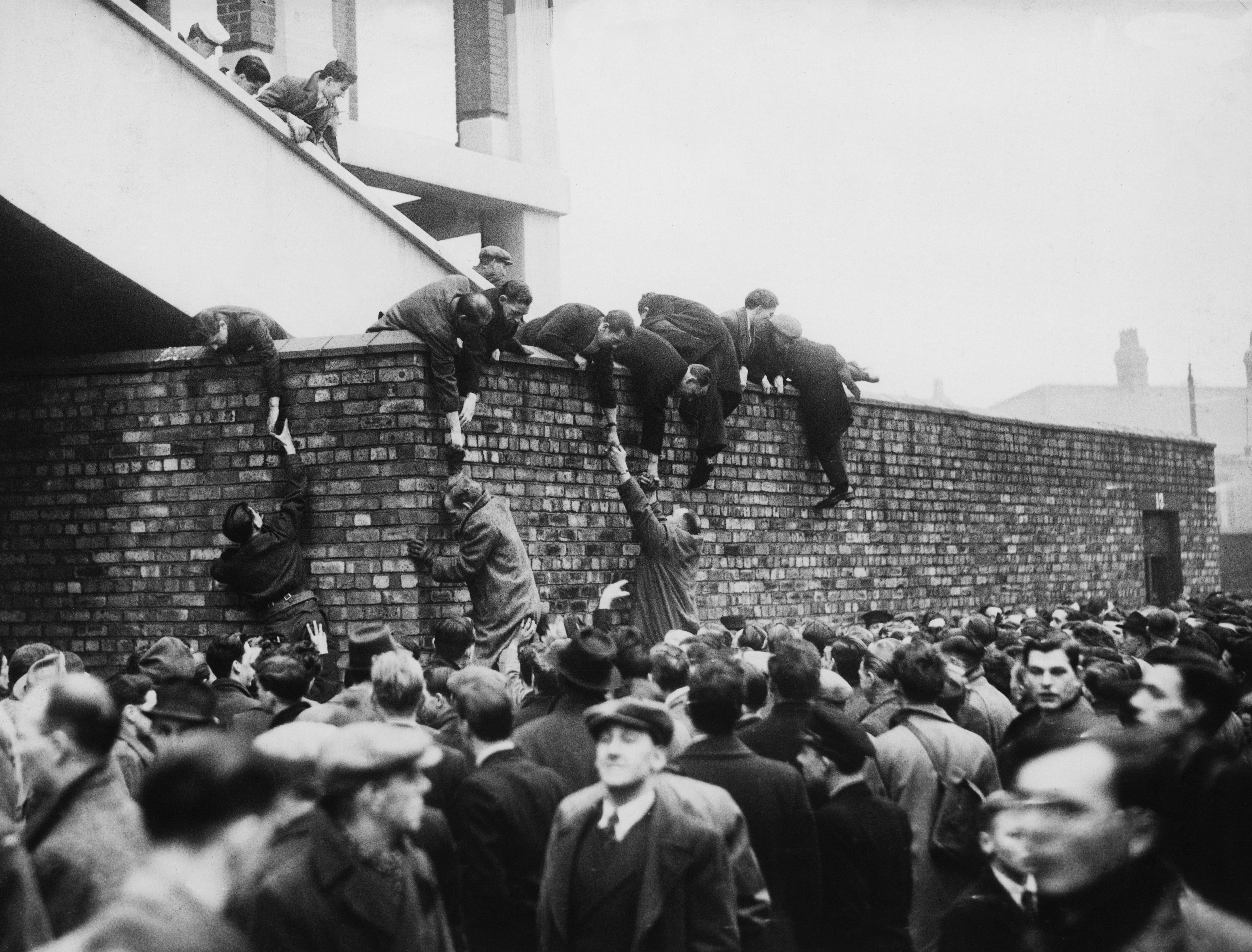 Football fans climb a wall to gain access to a game between Liverpool and Stoke City in December 1946.