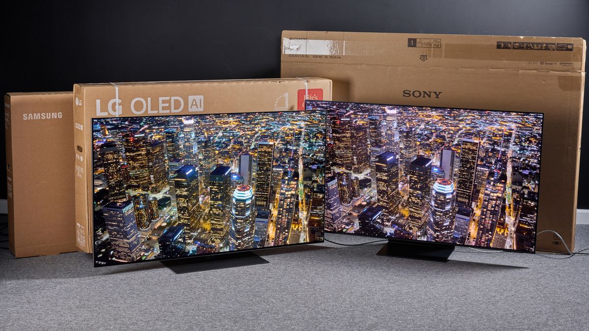 Two OLED TVs showing an aerial shot of a city at night on screen with cardboard boxes behind them