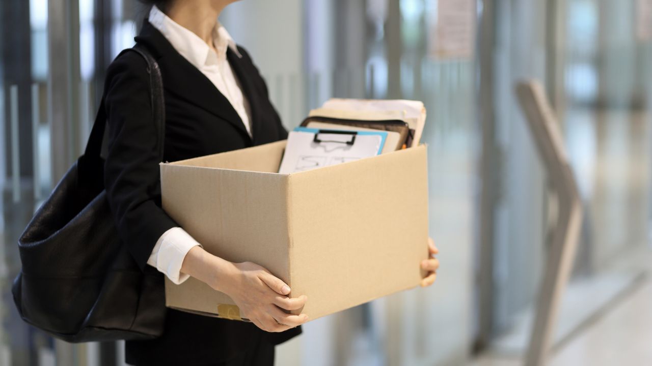 A woman carries a box of her belongings out of an office building.