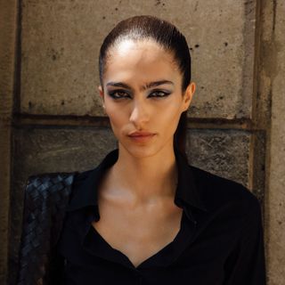 a model in Paris wearing a black shirt and heavy eye makeup, who has clear, glowing skin.