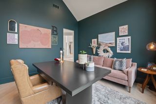 A home office with Sherwin-Williams' 'Cascades' paint on the walls, prints on the wall, a pink couch, and a beige sofa chair by a dark desk