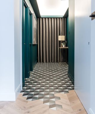 Light wooden chevron flooring and gray and white mosaic tiles laid next to each other in a hallway with green walls
