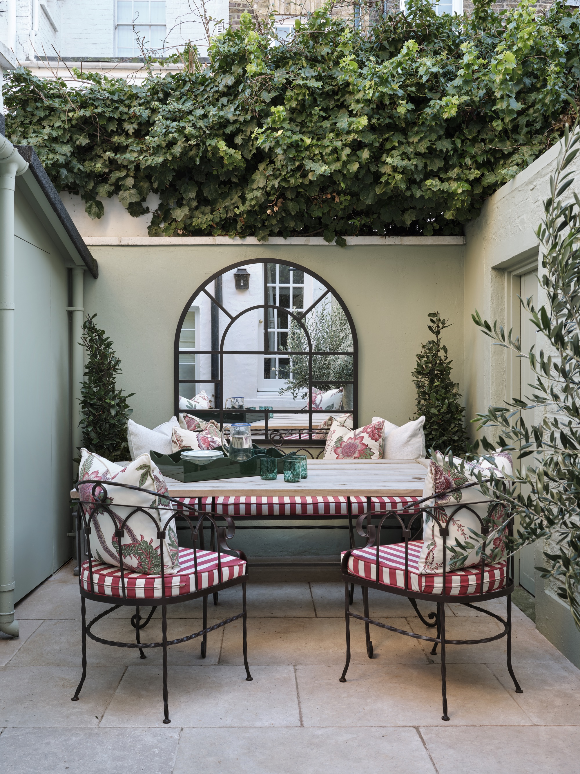 Courtyard garden with oversized arched window mirror and outdoor seating by Rosanna Bossom