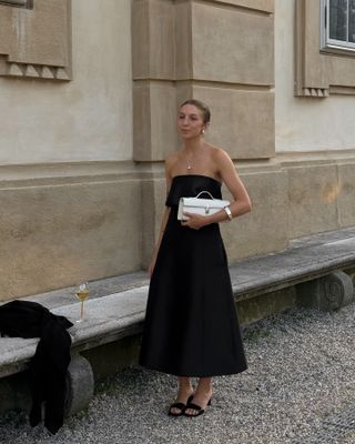 @brittanybathgate wearing a black midi dress, mules, and a Savette pochette bag.