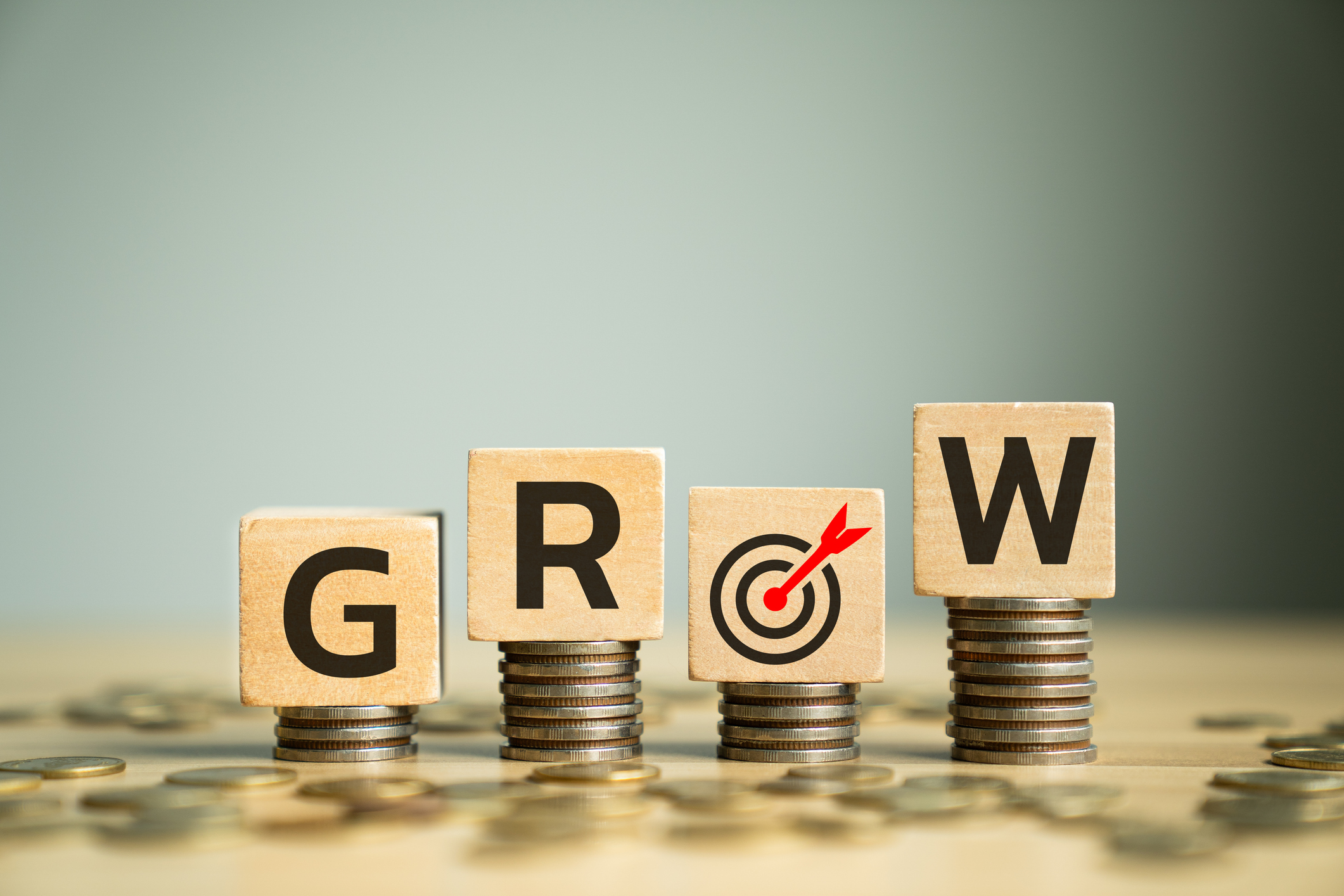 Wooden Block Letters Spelling GROW Placed on Stacked Coins with Target Symbol