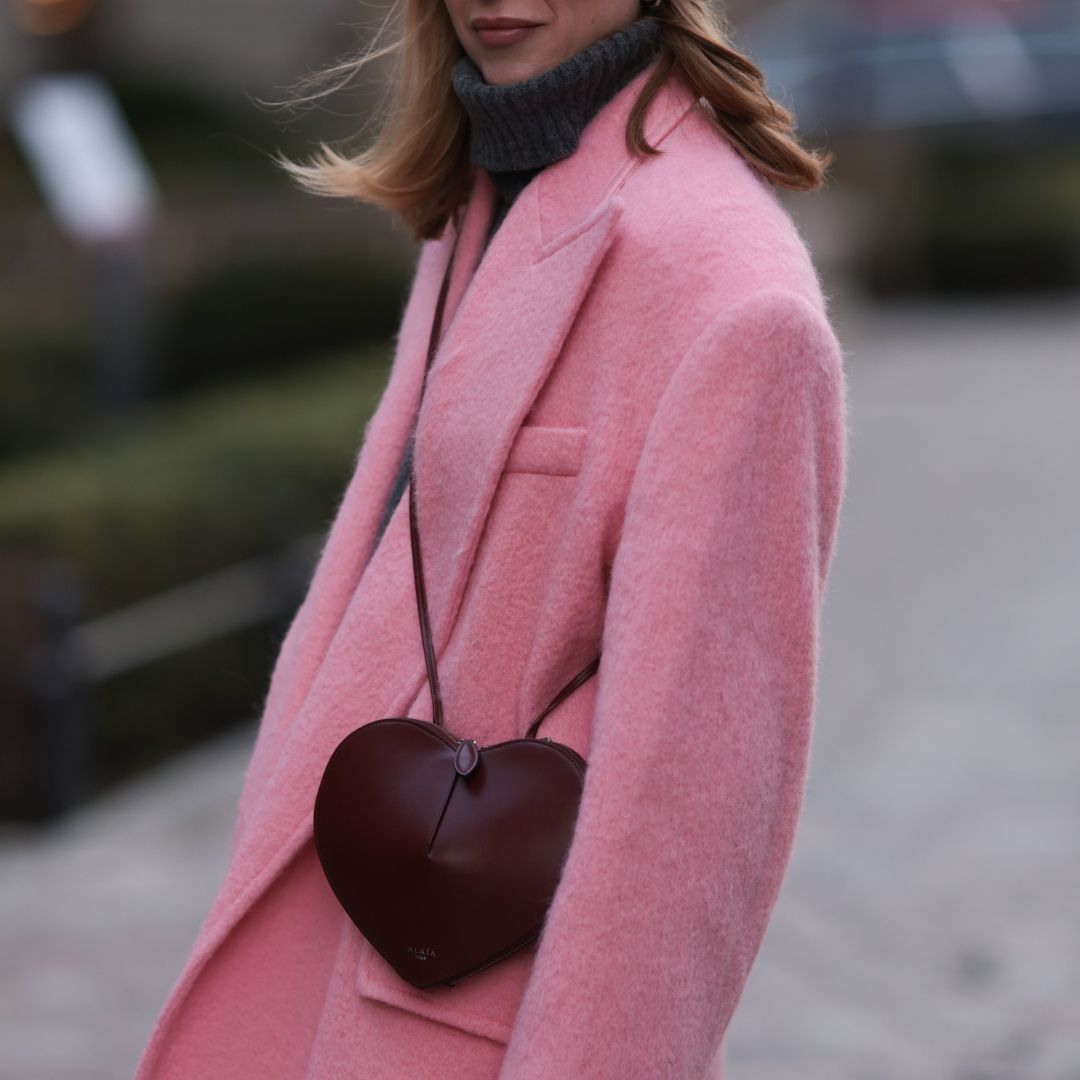 a woman wearing a pink coat and a burgundy heart bag in street style