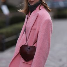 a woman wearing a pink coat and a burgundy heart bag in street style